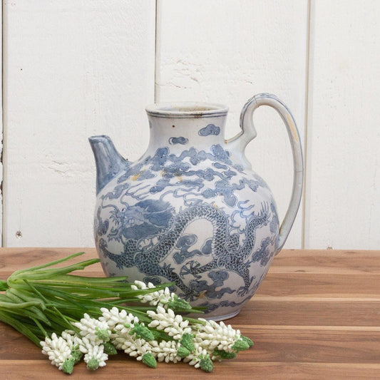 Blue and white ceramic pitcher with floral design on a wooden surface and white wooden background