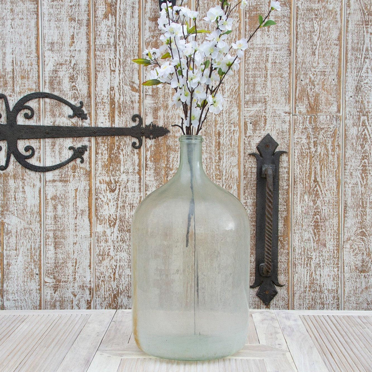 Clear glass bottle with white flowers against a wooden wall with metal brackets.