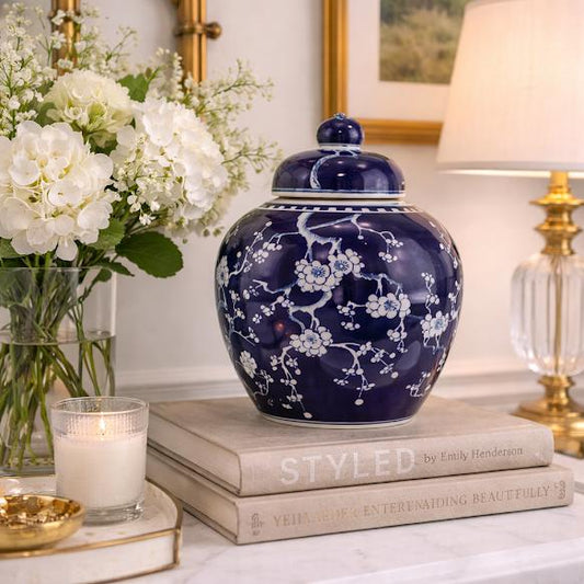 Decorative blue vase with white floral patterns on a table with books, flowers, and a lamp.