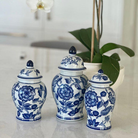 Three blue and white ceramic jars with floral designs on a marble surface, with white orchids in the background.