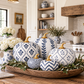 A styled arrangement of decorative pumpkins with blue and white geometric patterns and gold stems, displayed on a wooden tray in a bright, modern farmhouse kitchen.