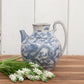 Blue and white ceramic pitcher with floral design on a wooden surface and white wooden background