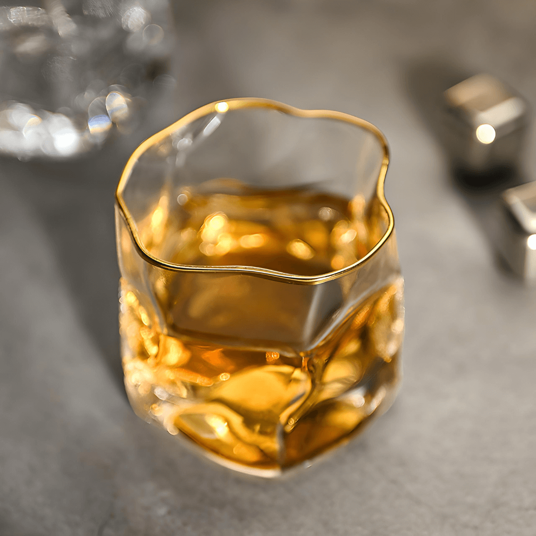 Glass of amber liquid with gold rim on a gray surface