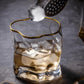 Glass of whiskey with ice being topped off with a gold-rimmed glass on a dark background