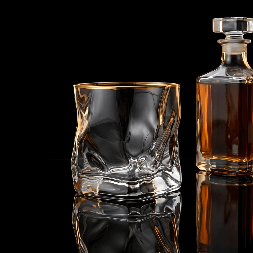 Clear glass whiskey glass and a decanter with liquid on a black background
