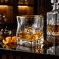 Glass of whiskey with ice cube on a bar counter with a decanter and garnishes.