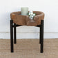 Small round table with a brown top and black legs on a textured surface with a white wall background.