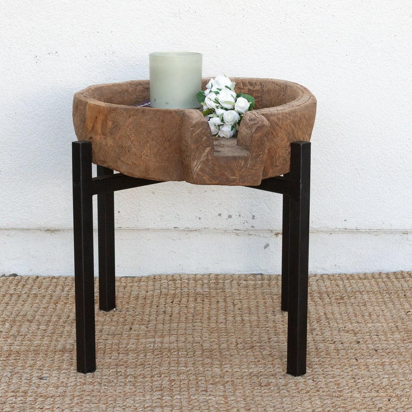 Small round table with a brown top and black legs on a textured surface with a white wall background.