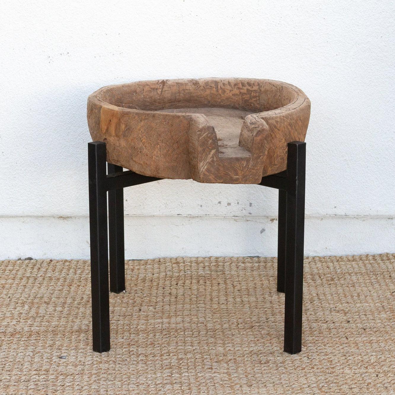 Round stone bowl on a black stand against a white wall.