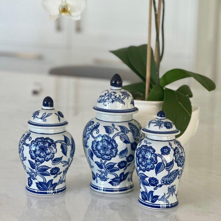 Three blue and white ceramic jars with floral designs on a marble surface, with white orchids in the background.